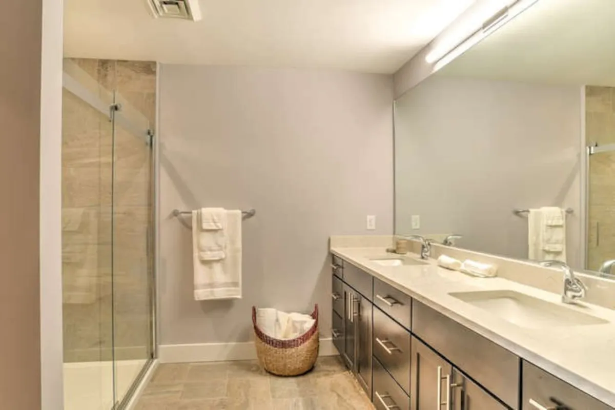 A contemporary bathroom is captured with a large wall mirror, double sink vanity, and a spacious glass shower. The layout and finishes evoke a spa-like experience, emphasizing room for relaxation and self-care.