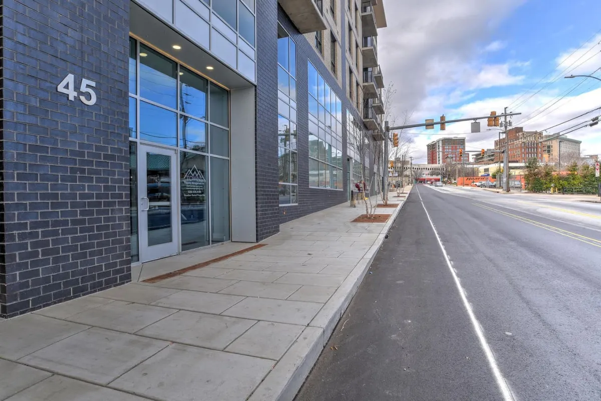 A street-level view of the building facade, featuring large windows and a clearly visible entrance door. The contemporary architecture stands out amidst the vibrant urban setting, and the sidewalk hints at easy pedestrian access to the heart of downtown.