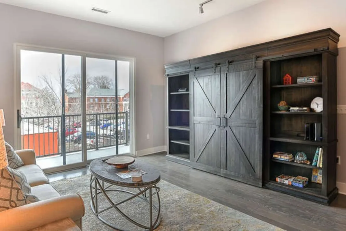 A welcoming interior shot of the living space featuring a cozy sofa, coffee table, bookshelves, and a balcony view. The space feels inviting and comfortable, and the balcony doors hint at a seamless transition from inside the sanctuary to the downtown energy outside.